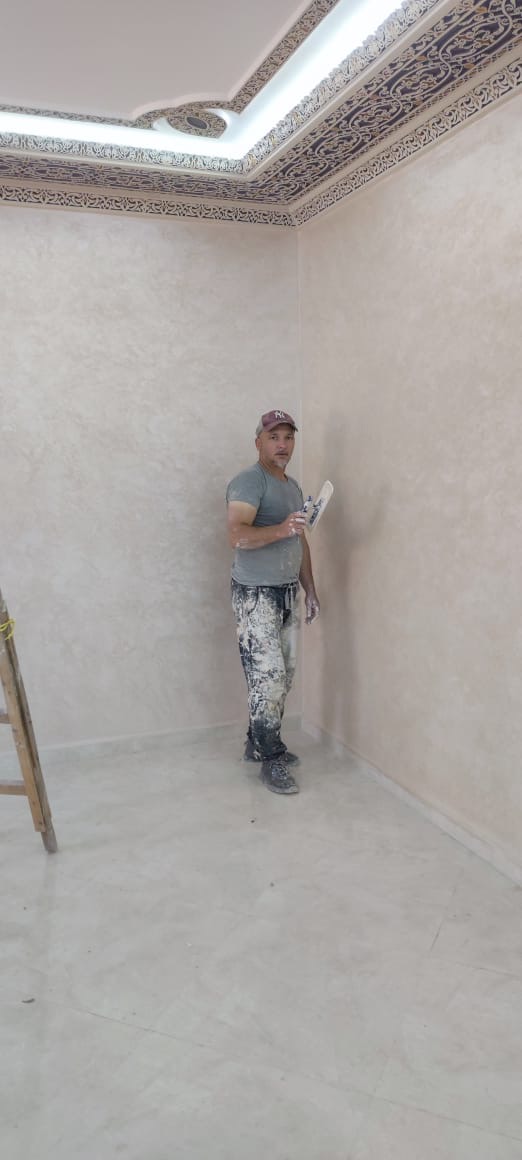L'artisan appliquant un enduit décoratif sous un plafond à frise marocaine